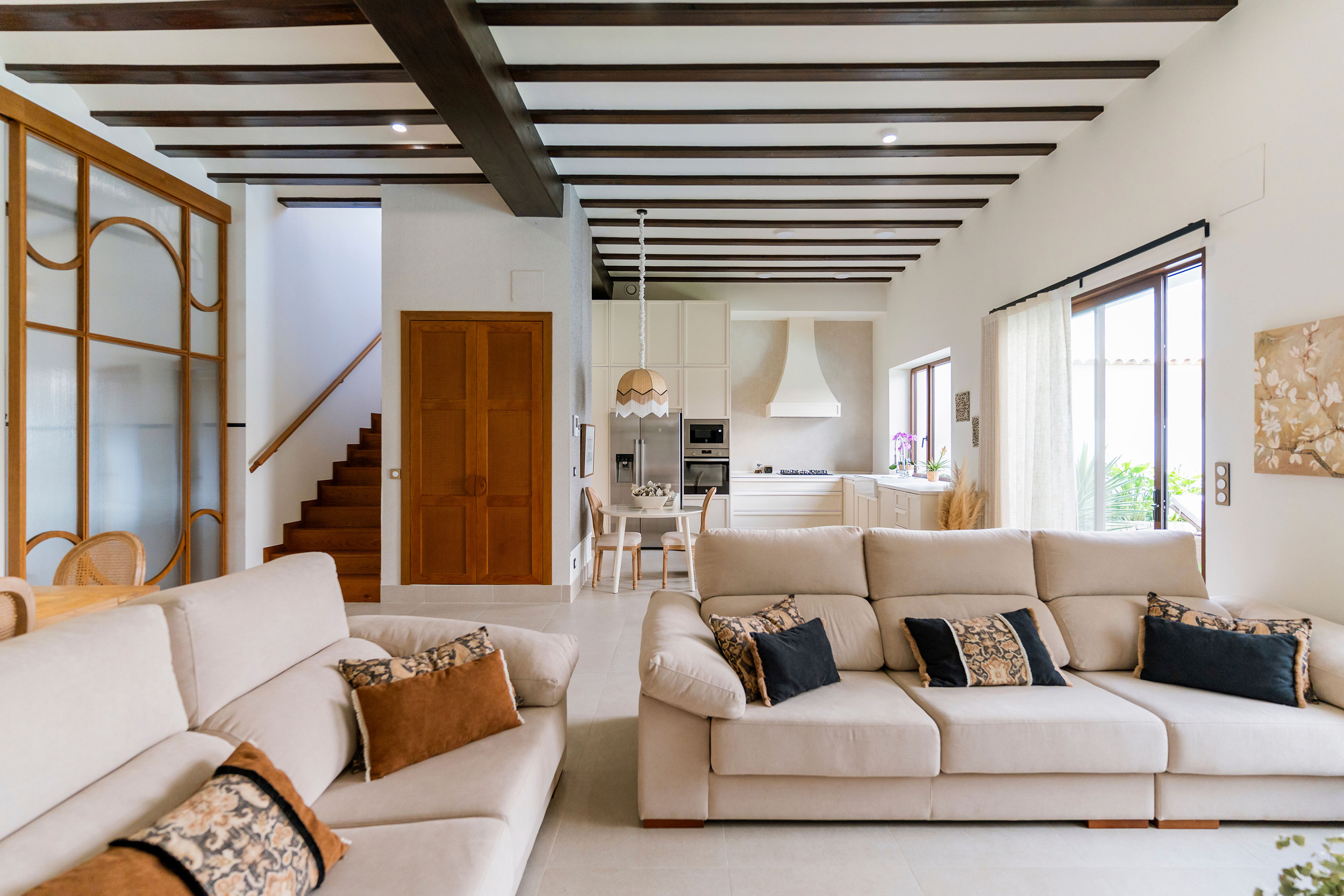 Rehabilitación interior de Casa Sofia: salón comedor abierto a la cocina, con vigas de madera vistas y luz natural.