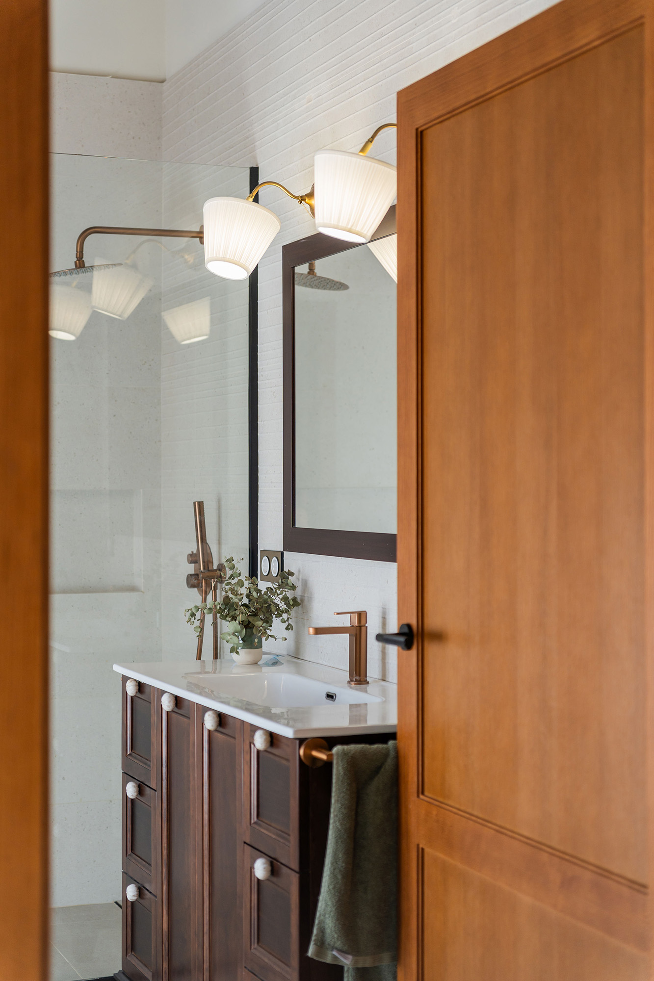Baño reformado de Casa Sofia con ducha a ras de suelo, revestimientos claros, mueble de madera y techo con vigas vistas.